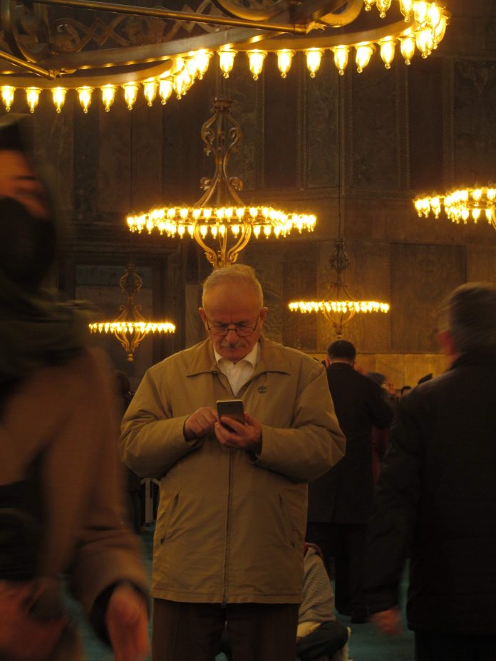 Elderly Man with Phone Standing Under Chandelier in Church Elderly Man with Phone Standing Under Chandelier in Church